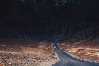 Empty road amidst trees against mountains