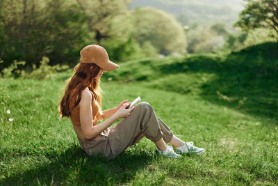 Side view of woman sitting on grassy field