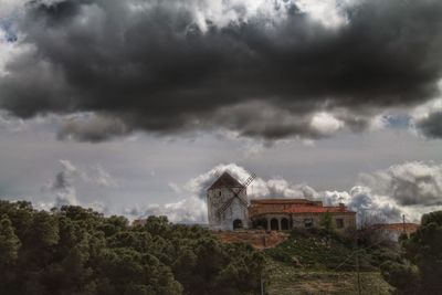 Traditional windmill by house against cloudy sky