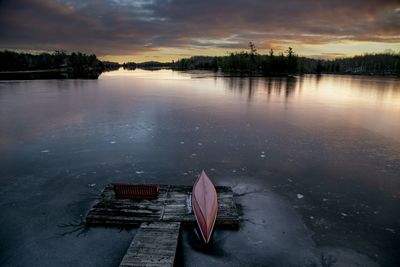 Pastel sunrise colors reflected on ice surface on a lake with a red canoe