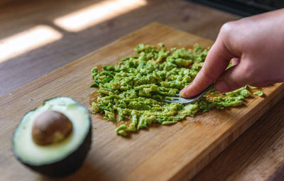Close-up of person preparing mashed avocado on wooden cutting board