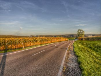 Empty road amidst field against sky