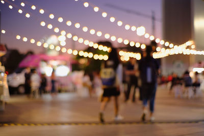 Defocused image of people walking on illuminated street at night