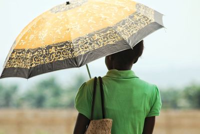 Rear view of woman with umbrella standing against sky