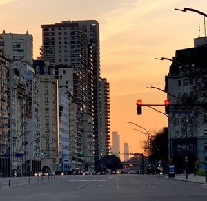 City street by buildings against sky during sunset