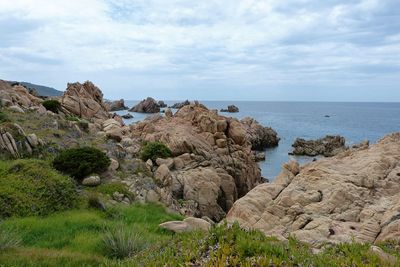 Rock formations on coast against cloudy sky