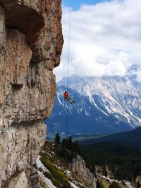 Low angle view of man rappelling by rocky mountain against sky