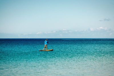 Rear view of man paddleboarding in sea against sky