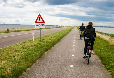 Rear view of man riding bicycle on road against sky