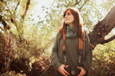 Low angle view of young woman with camera standing in forest