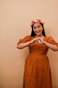 Portrait of young woman standing against nude color background