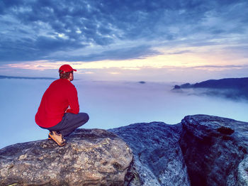 Man lost in thick mist rocks. hiker climbed up alone to exposed summit above fog. big adventure