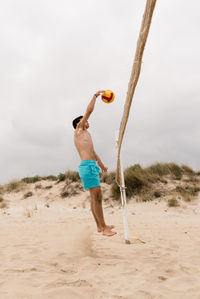 Full length of shirtless man holding umbrella on beach
