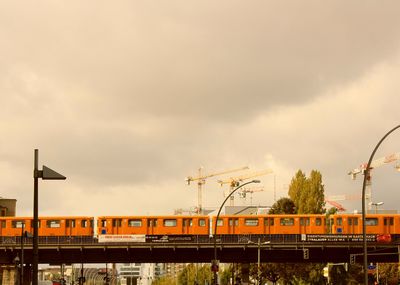 Train on railway bridge in city against cloudy sky
