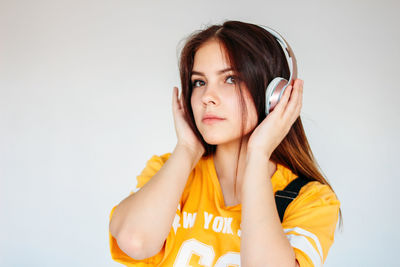 Close-up of beautiful young woman wearing headphones against gray background