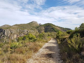 Footpath leading towards mountains against sky