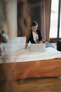 Businesswoman using laptop on bed in hotel room