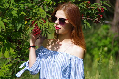 Young woman wearing sunglasses while standing by tree