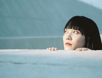 Woman looking away while standing by wall at seaside