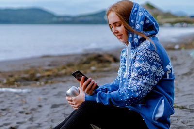 Young woman using phone while sitting at beach