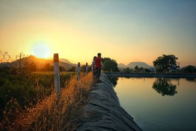 Friends standing by lake against sky during sunset