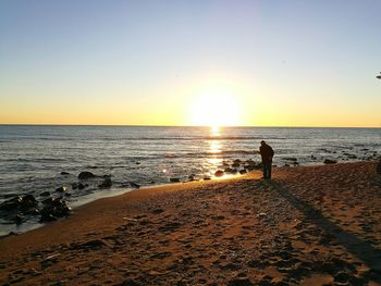 Silhouette man on beach against clear sky during sunset
