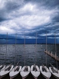 Boats moored in sea against cloudy sky