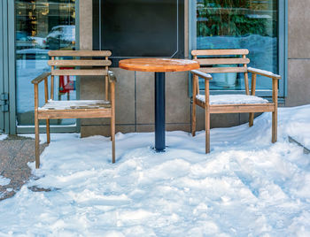 Table and chairs of a street cafe in winter is covered with snow.