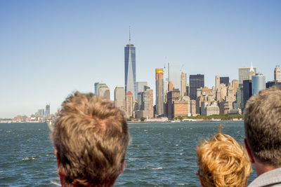 Rear view of people standing against sea and cityscape against clear sky