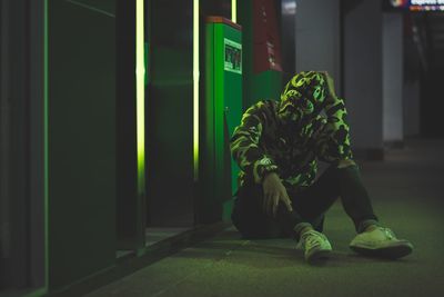 Man wearing mask while sitting in corridor at night