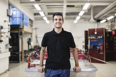 Portrait of happy male auto mechanic student standing in workshop