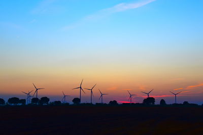 Silhouette of wind turbines on field against sky during sunset