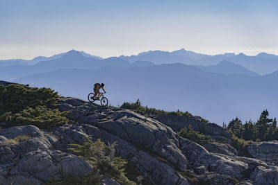 Hiker riding bicycle on mountain against sky