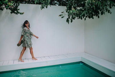 Woman standing by swimming pool against wall