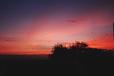 Silhouette trees on landscape against romantic sky at sunset