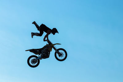 Low angle view of man jumping against clear blue sky