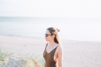 Woman wearing swimwear standing at beach against sky