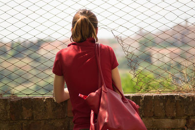 Rear view of girl standing on chainlink fence in front of sea