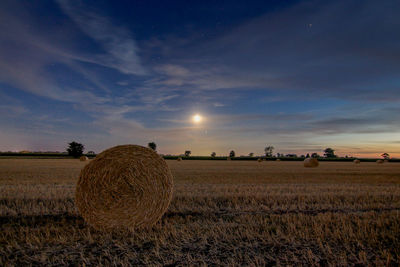 Hay bales on field against sky during sunset