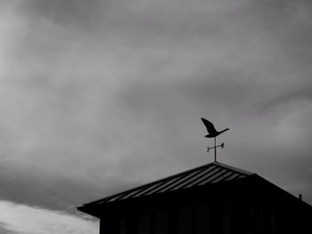 Low angle view of weather vane against cloudy sky