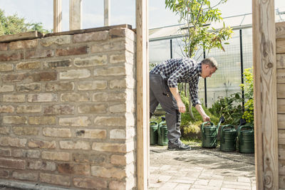 Side view of man picking watering can at greenhouse