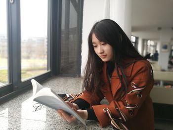 Young woman reading book at window sill