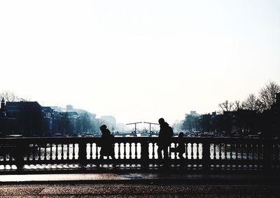 Silhouette men on bridge against clear sky