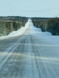 Snow covered road by trees against sky