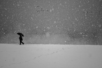 Silhouette man with umbrella walking on landscape during snowfall