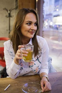 Smiling young woman having drink while sitting at restaurant table