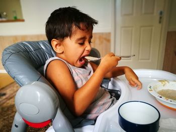 Boy eating food with spoon at home