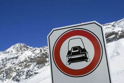 Road sign on snowcapped mountain against clear blue sky