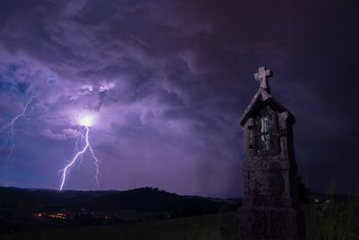 Old cross on field against lighting in sky at night