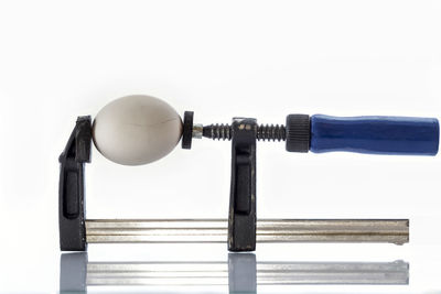 Close-up of egg and work tool against white background